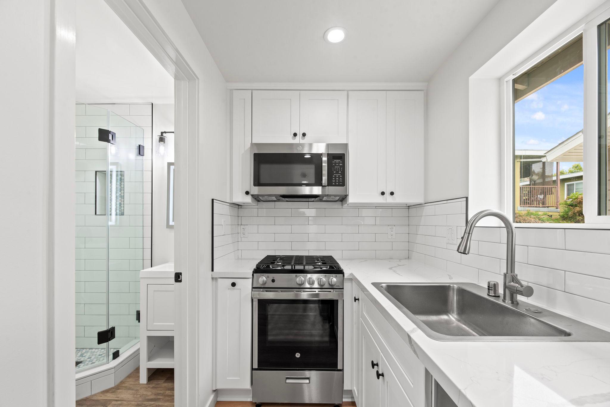 Kitchenette with quartz counters and subway tile, with the bathroom beyond (after)