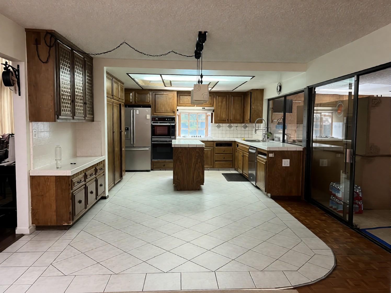 Before: the old kitchen with brown wood cabinets, tile countertops, a skylight and a chain-hung light over the island