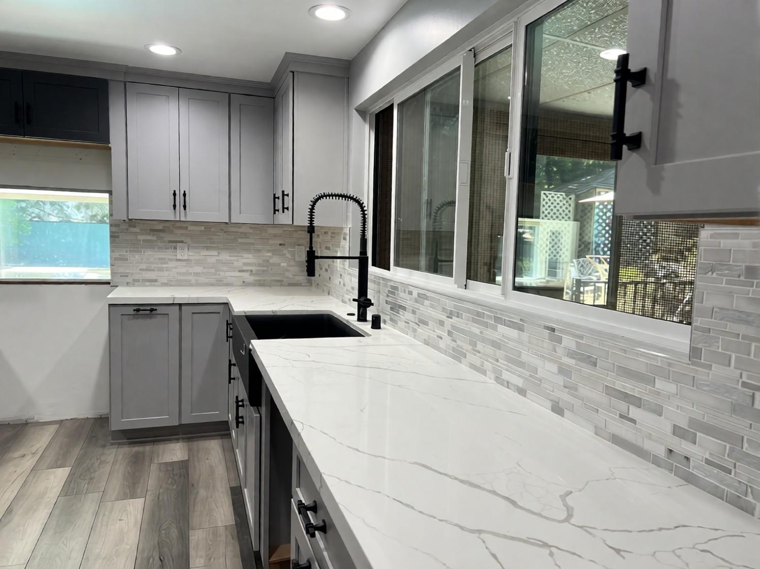 Black farmhouse sink with a matte black pull-down faucet, countertop and mosaic backsplash detail